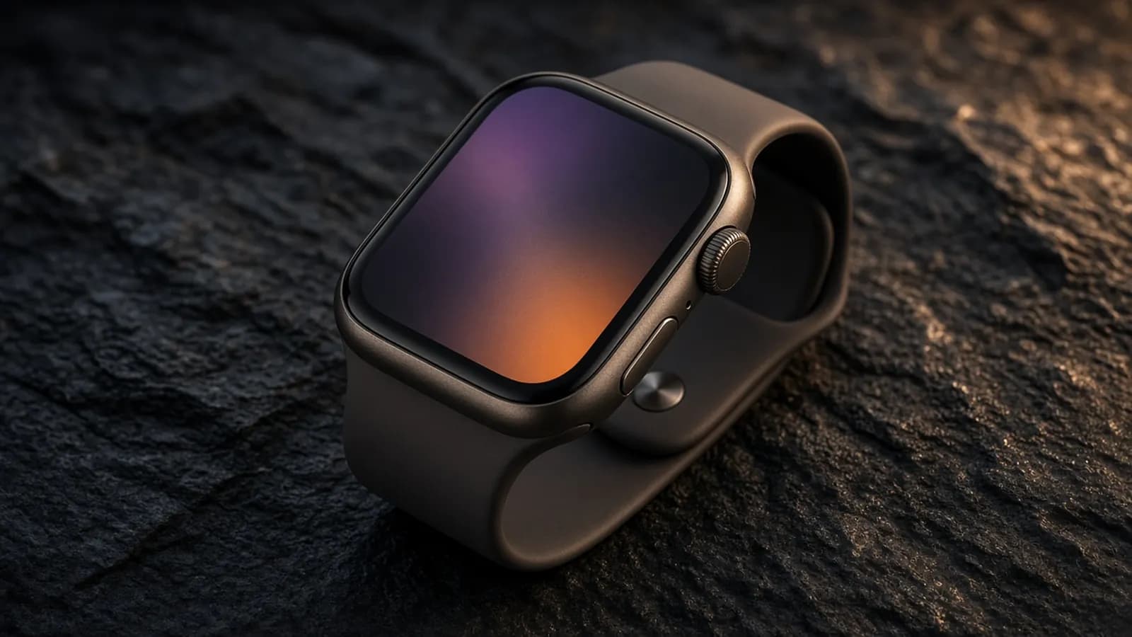 A rectangular smartwatch with a dark bronze aluminum case and matching sport band resting on a charcoal stone surface