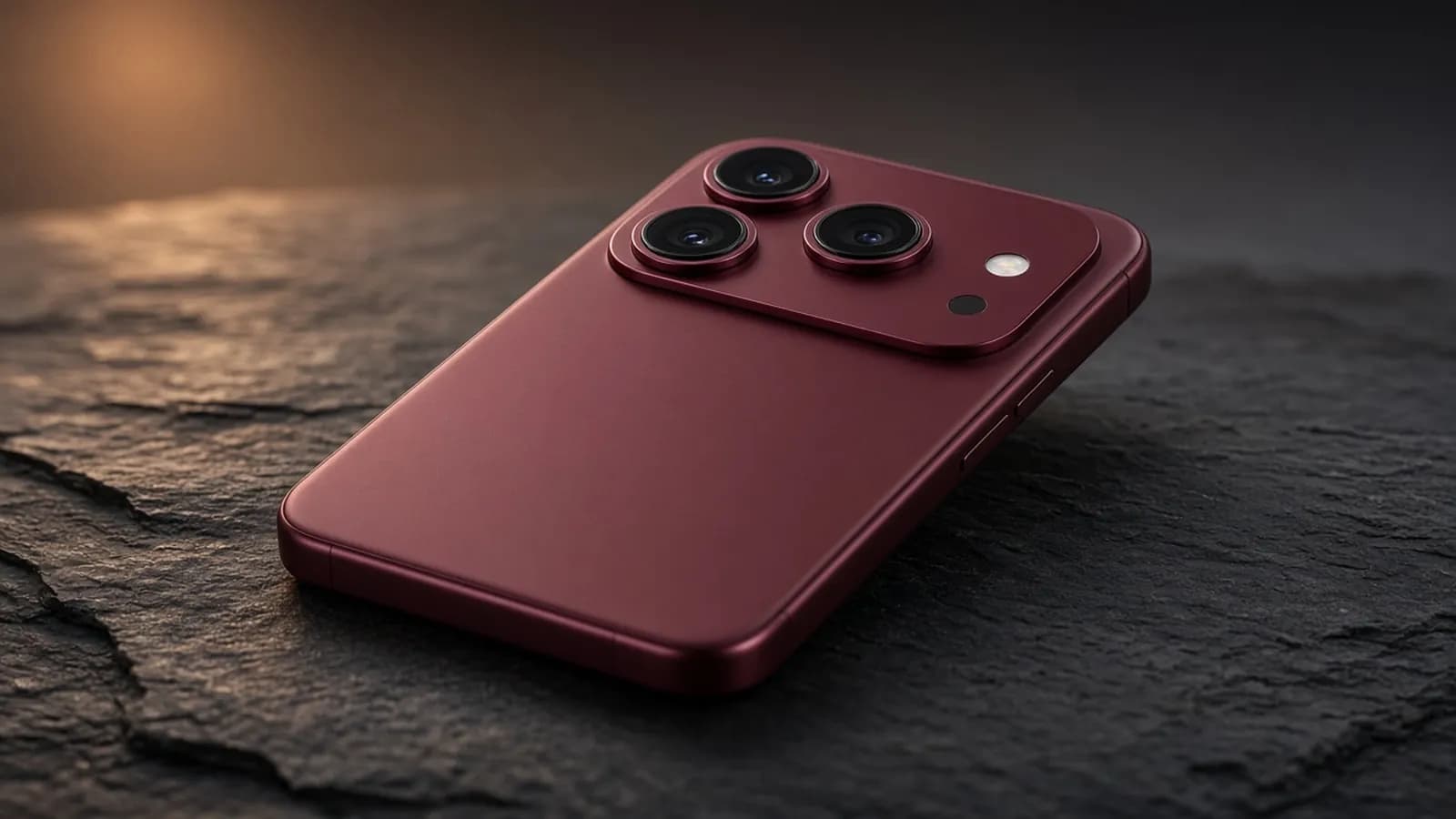 Burgundy flagship smartphone with a full-width triple-lens camera plateau lying on a dark slate surface
